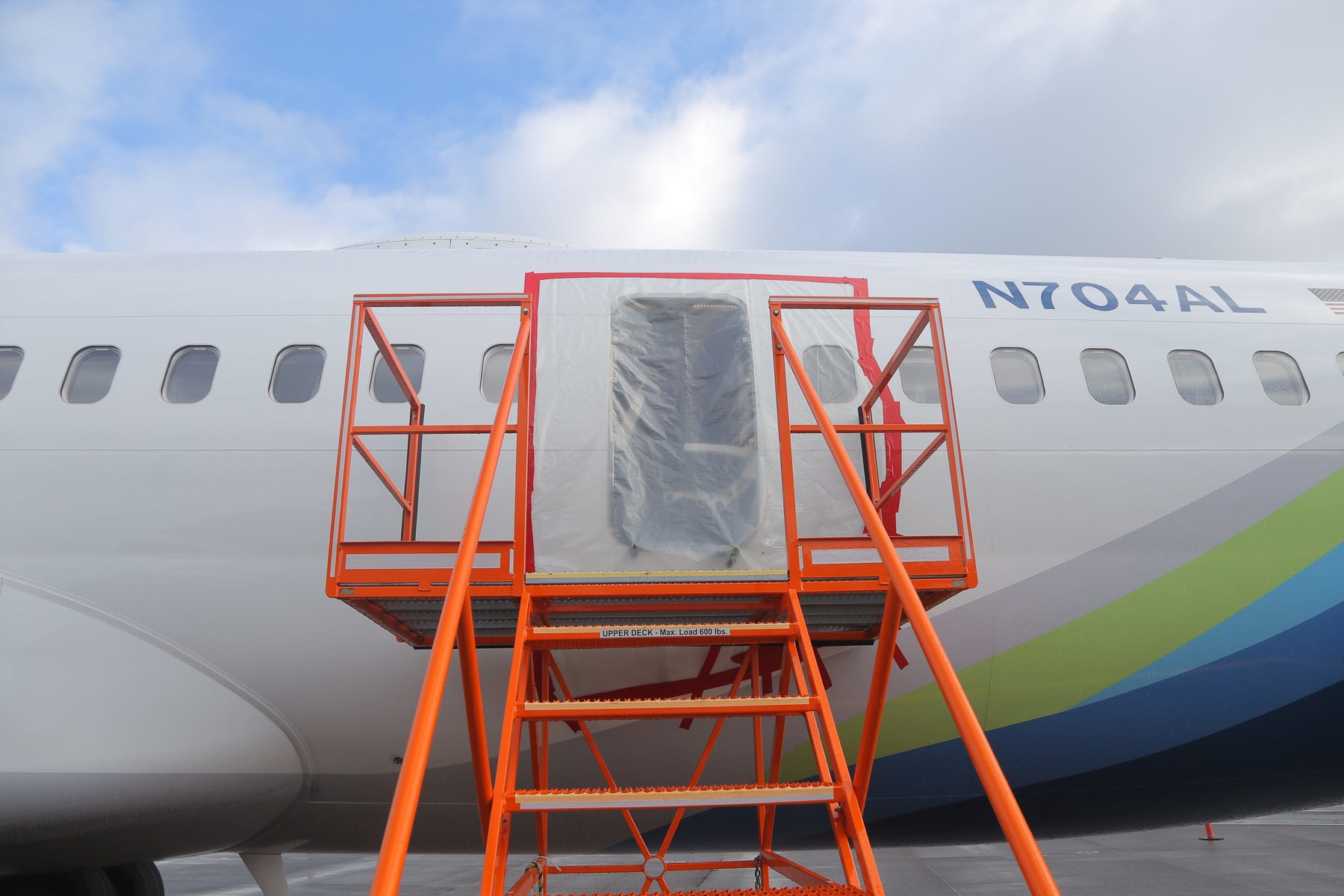 The fuselage of Alaska Airlines Boeing 737-9 N704AL at Portland International Airport, January 7, 2024, showing the plastic-covered opening where the mid-exit door plug separated in flight. Photo: National Transportation Safety Board (public domain).